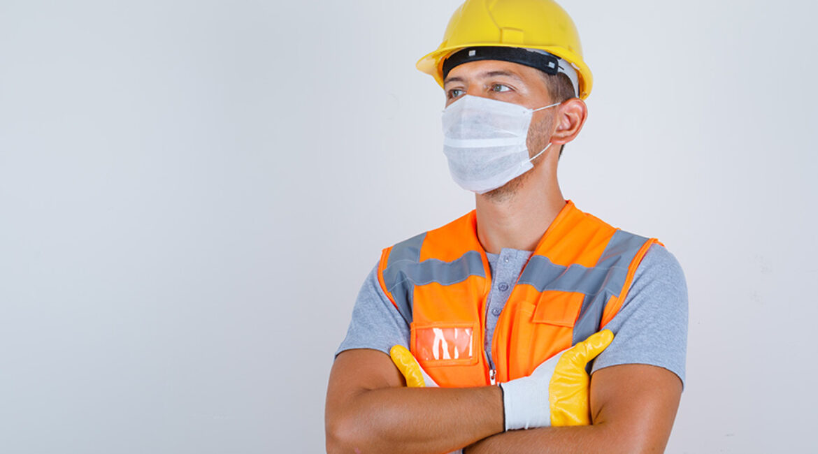 Male builder in uniform, helmet, gloves, mask looking away with