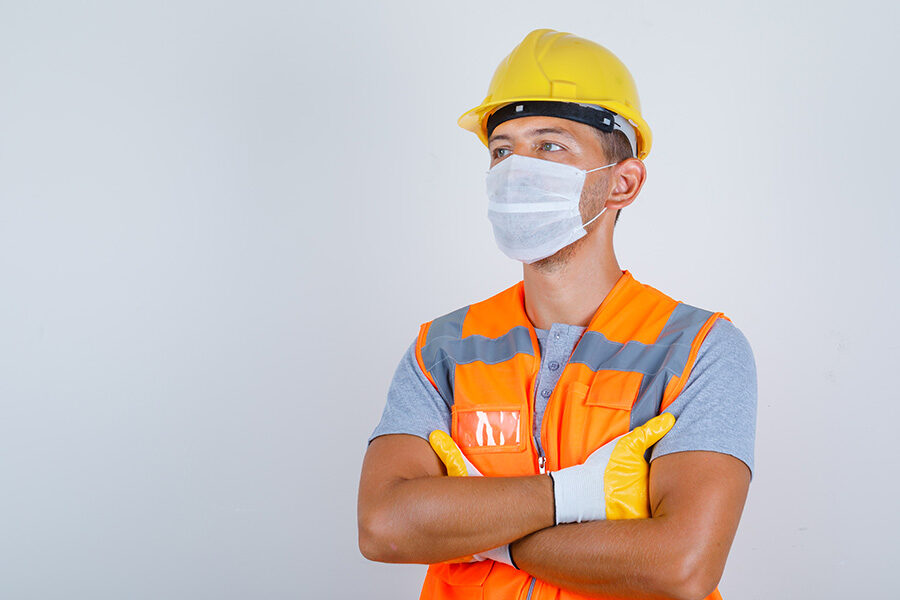 Male builder in uniform, helmet, gloves, mask looking away with