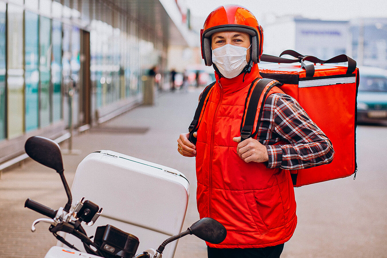 Food delivery boy driving scooter with box with food and wearing mask